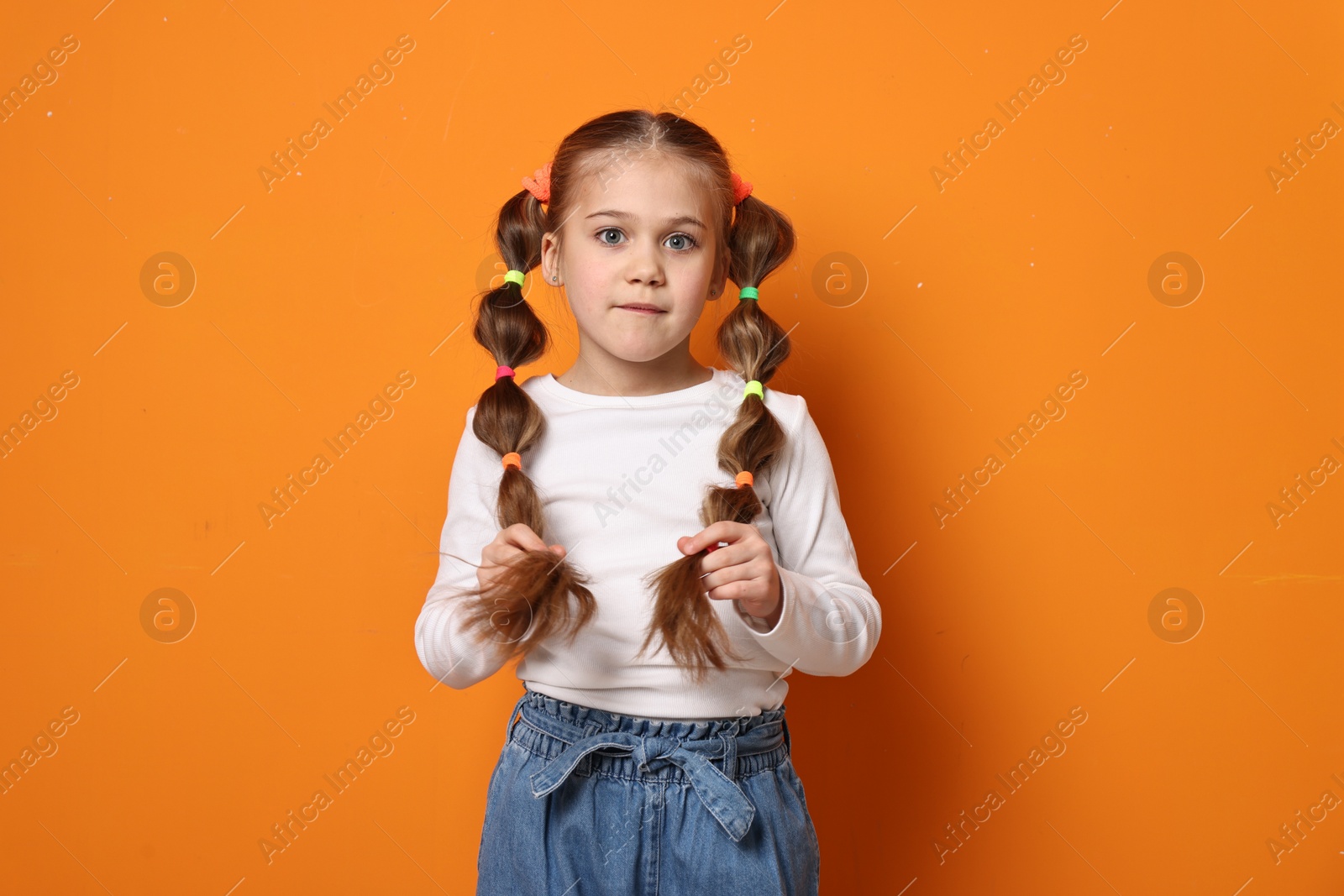 Photo of Cute little girl with beautiful hairstyle on orange background