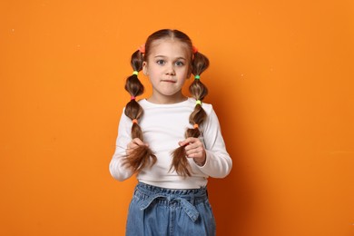 Cute little girl with beautiful hairstyle on orange background