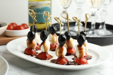 Tasty canapes with black olives, mozzarella and cherry tomatoes on white marble table, closeup