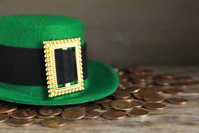 Photo of Green leprechaun hat and gold coins on wooden table, space for text. St. Patrick's Day celebration