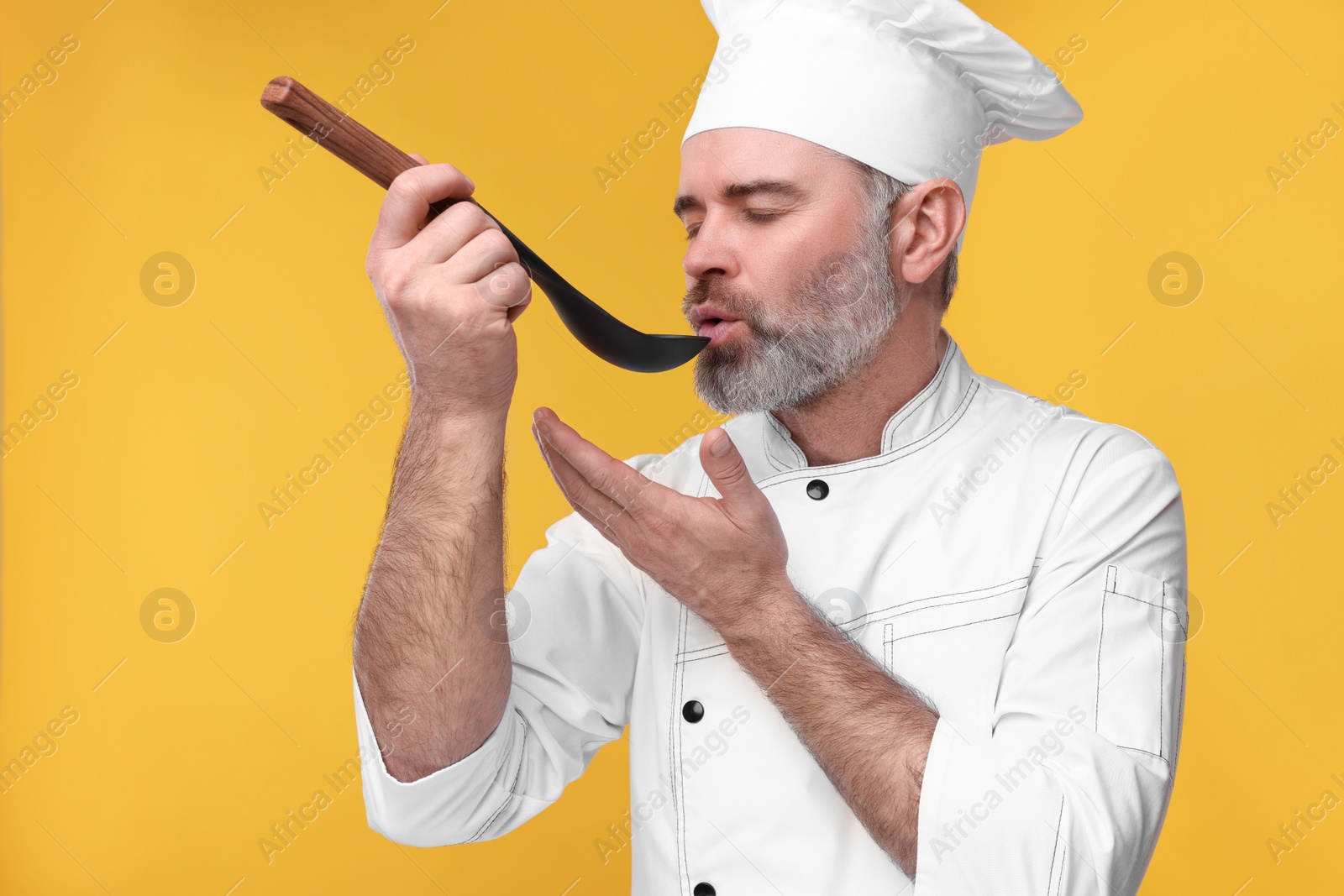 Photo of Chef in uniform tasting something on orange background