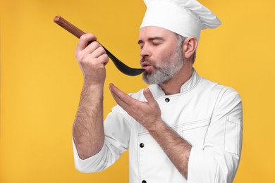 Photo of Chef in uniform tasting something on orange background