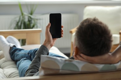 Photo of Man using smartphone at home, focus on hand with gadget