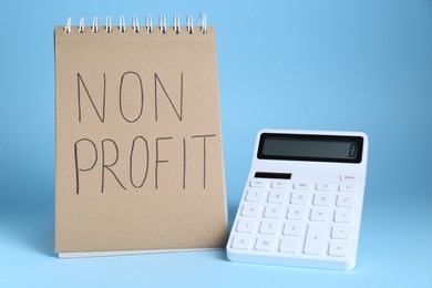 Photo of Notebook with phrase Non Profit and calculator on light blue background