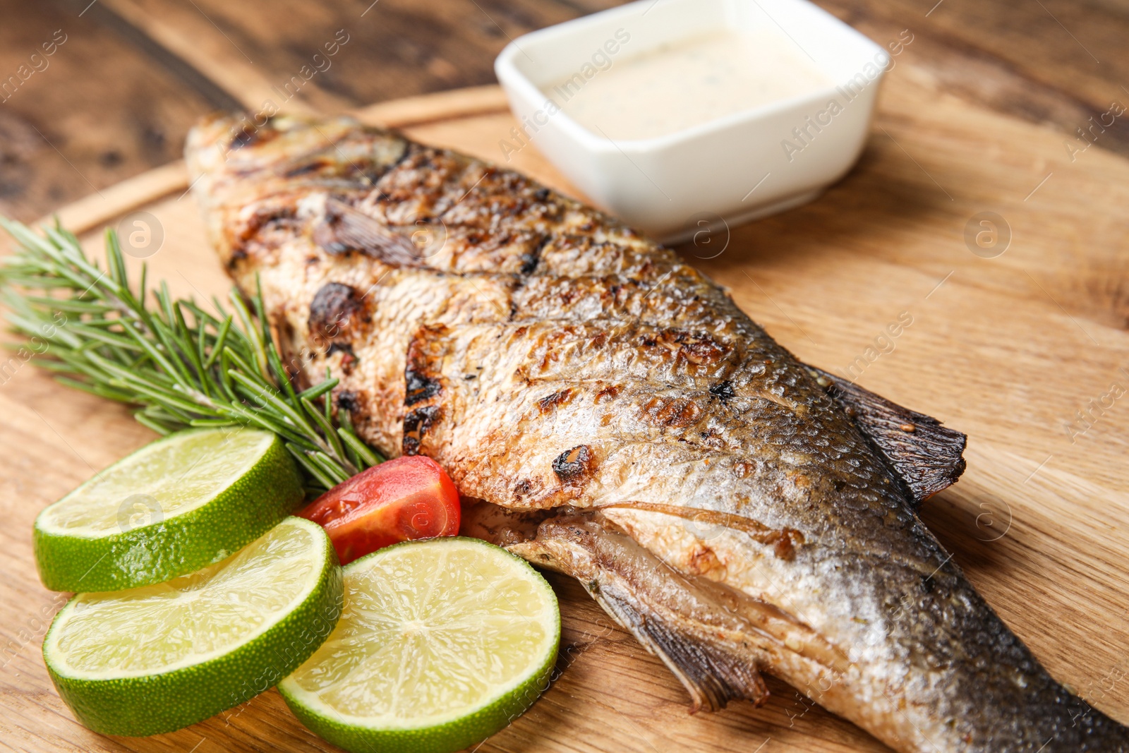 Photo of Delicious grilled fish with lime on wooden board, closeup