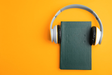 Book and modern headphones on yellow background, top view. Space for text