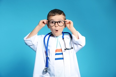 Photo of Cute child in doctor coat with stethoscope on color background