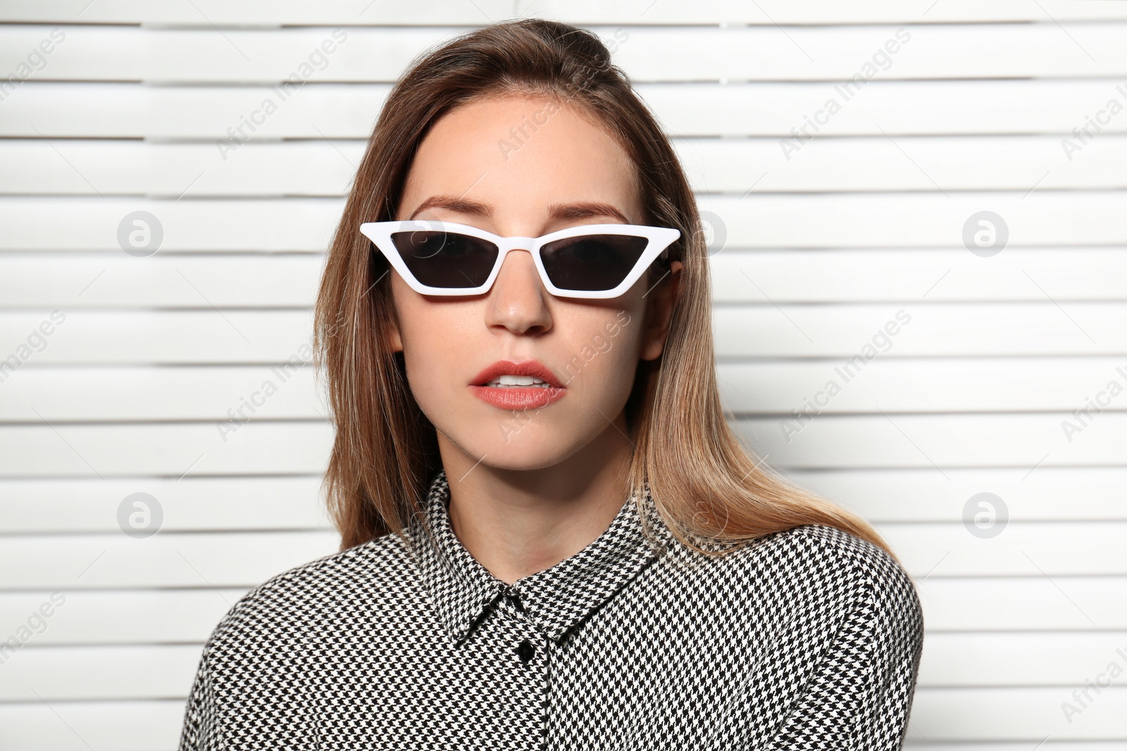 Photo of Young woman wearing stylish sunglasses against blinds