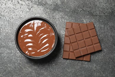 Photo of Tasty milk chocolate paste in bowl and bars on gray table, top view