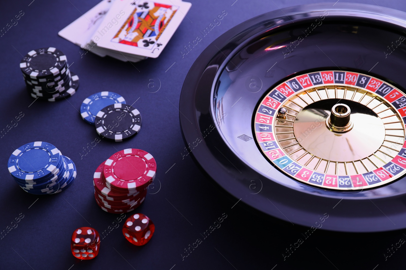 Photo of Roulette wheel, playing cards and chips on table, closeup. Casino game