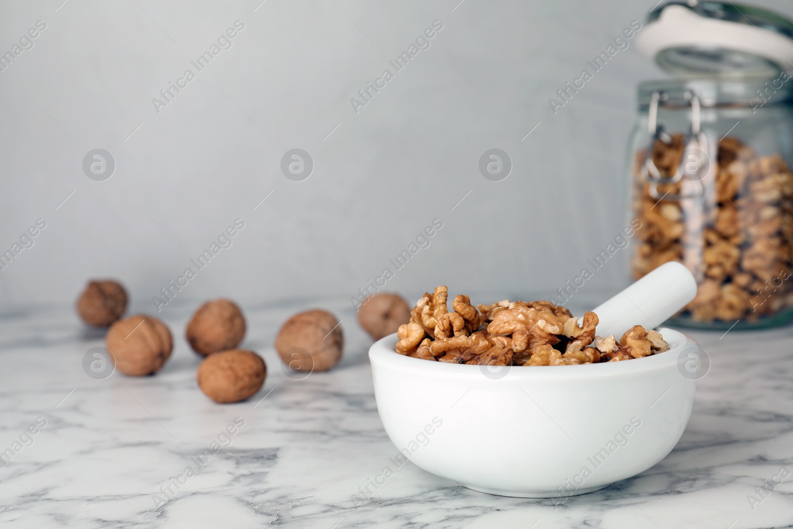 Photo of Mortar with walnuts and pestle on marble table. Space for text