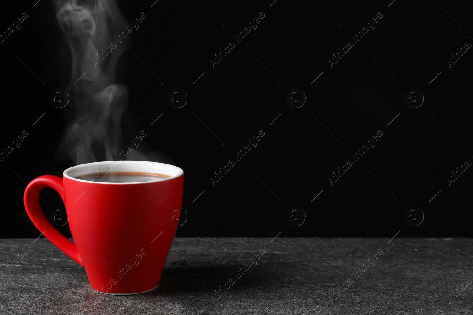 Image of Red cup with hot steaming coffee on grey table against black background, space for text