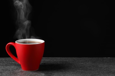 Image of Red cup with hot steaming coffee on grey table against black background, space for text