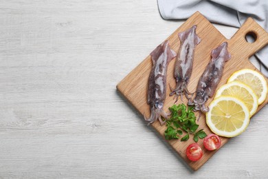 Photo of Fresh raw squids with lemon, parsley and tomato on white wooden table, top view. Space for text