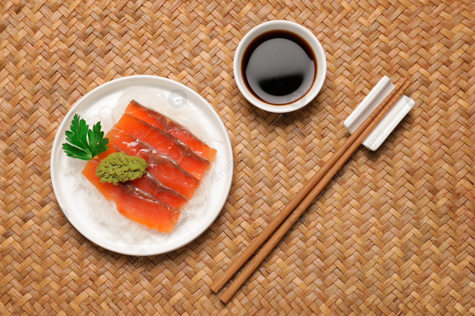Photo of Sashimi set (raw salmon slices) served with funchosa, parsley, vasabi and soy sauce on wicker surface, flat lay