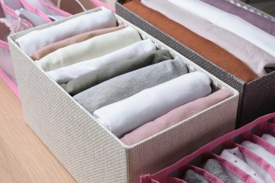 Photo of Textile cases with folded clothes on wooden background, closeup. Vertical storage