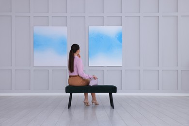 Young woman at exhibition in art gallery, back view