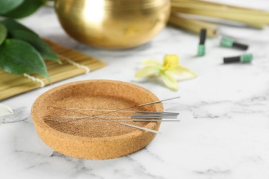 Cork plate with acupuncture needles on white marble table
