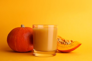 Tasty pumpkin juice in glass, whole and cut pumpkins on orange background