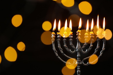 Photo of Silver menorah with burning candles against dark background and blurred festive lights, space for text. Hanukkah celebration