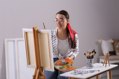 Photo of Happy woman artist drawing picture on canvas indoors