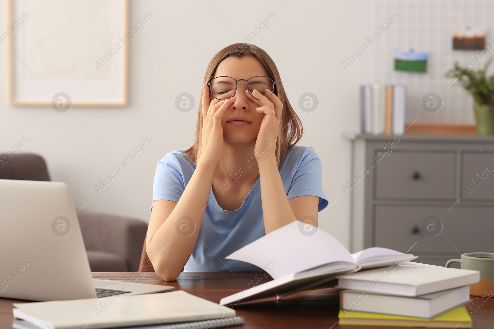 Photo of Young tired woman studying at wooden table in room