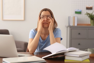 Young tired woman studying at wooden table in room