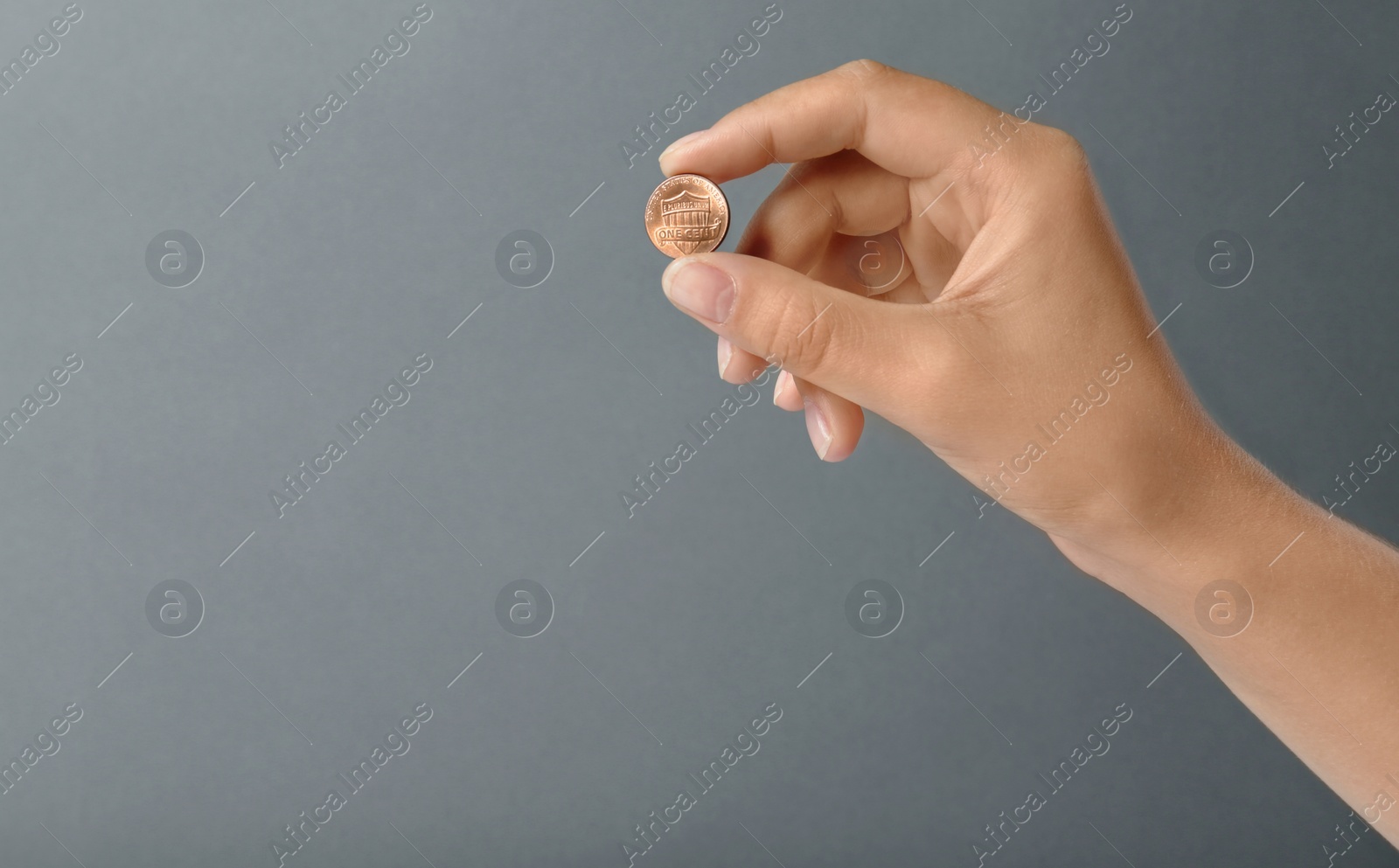 Photo of Young woman holding coin on grey background, closeup. Space for text