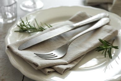 Stylish setting with cutlery, napkin, rosemary and plate on table, closeup