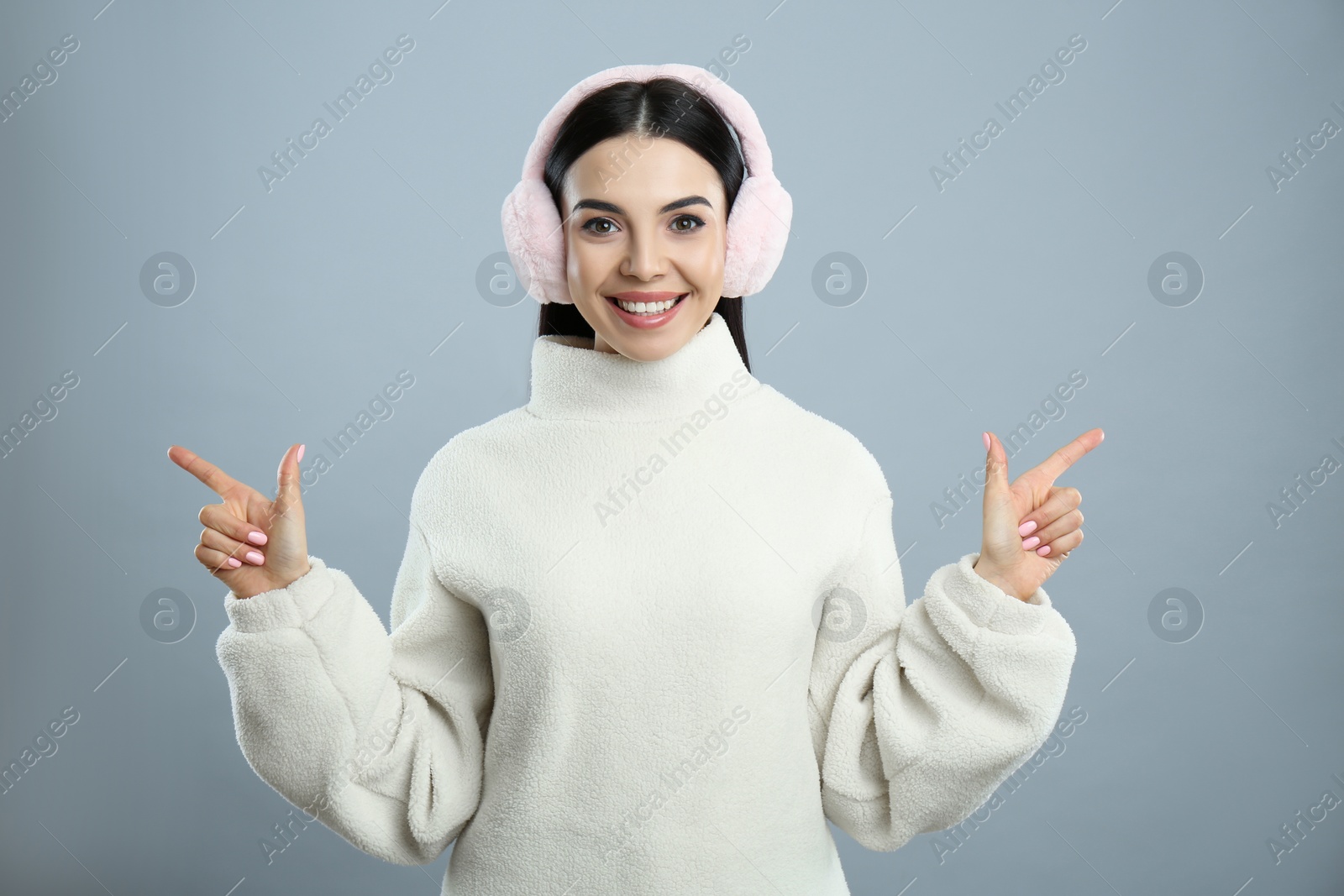 Photo of Beautiful young woman wearing earmuffs on light grey background