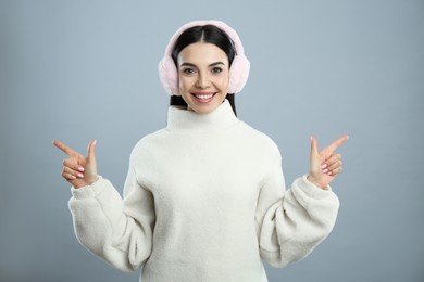 Beautiful young woman wearing earmuffs on light grey background