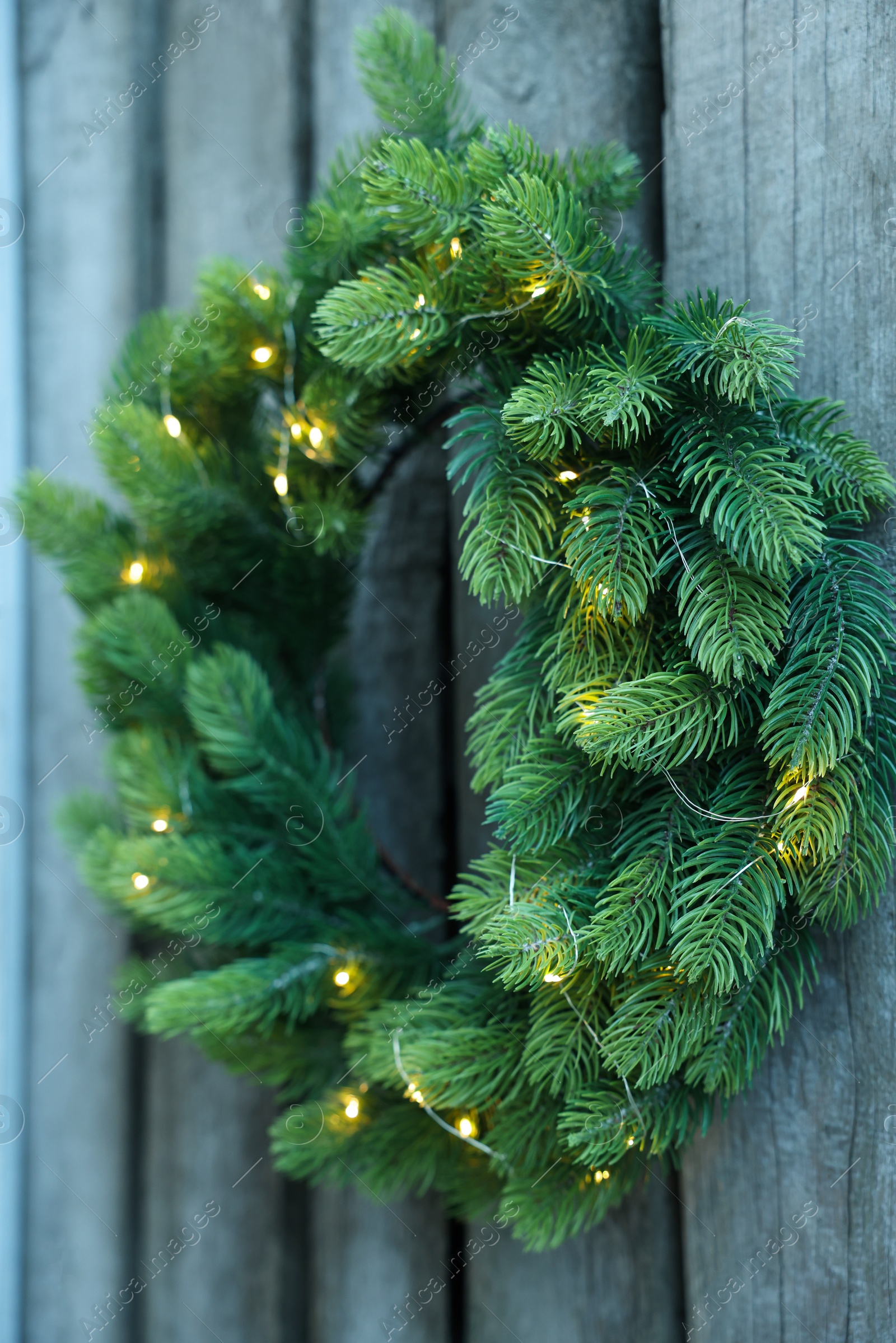 Photo of Beautiful Christmas wreath with string lights hanging on wooden wall