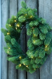 Beautiful Christmas wreath with string lights hanging on wooden wall