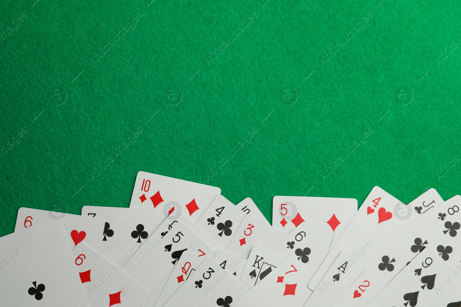 Photo of Scattered playing cards on green table, top view. Space for text