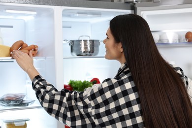 Young woman taking sausages out of refrigerator, back view