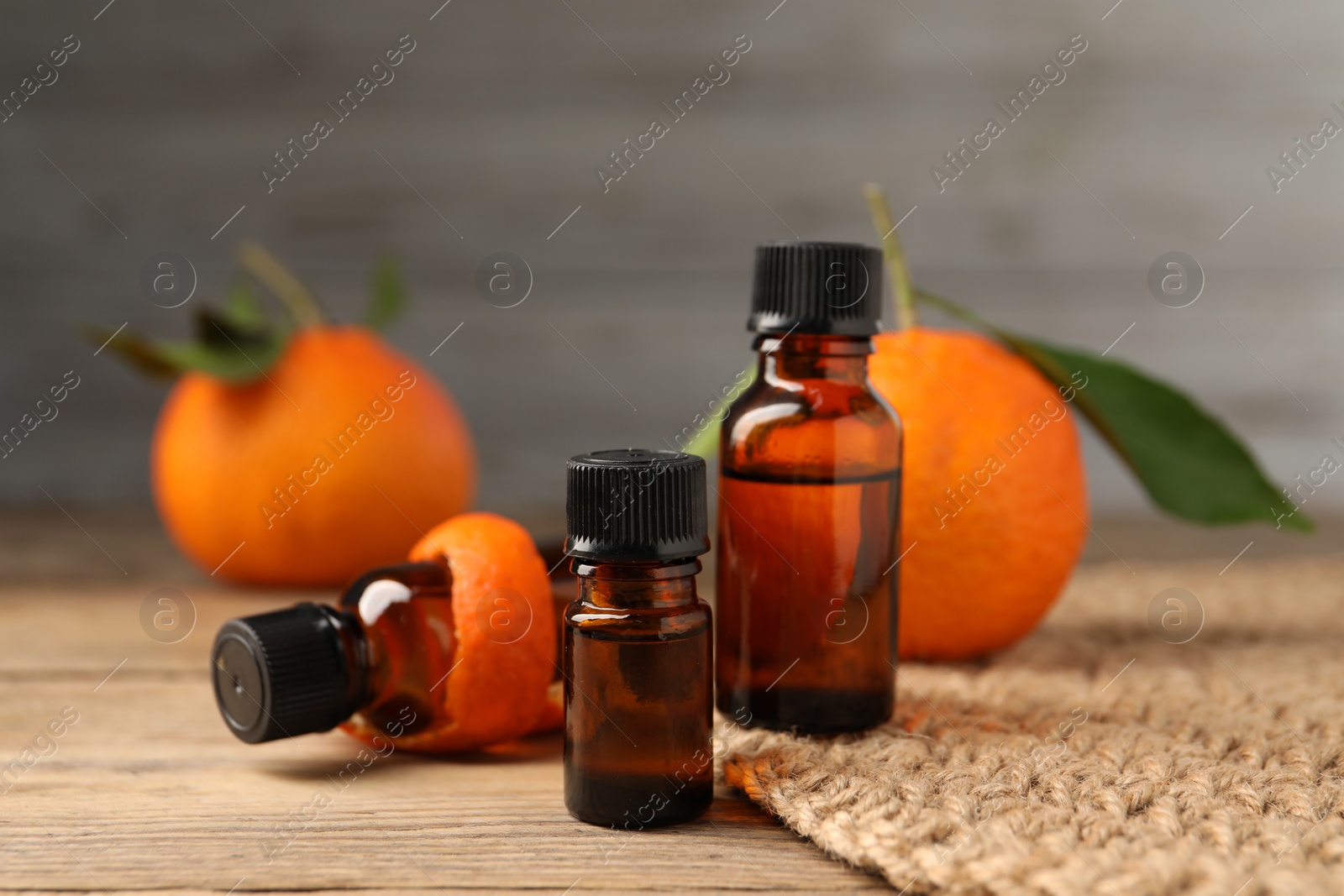 Photo of Bottles of tangerine essential oil, fresh fruit and peel on wooden table, closeup
