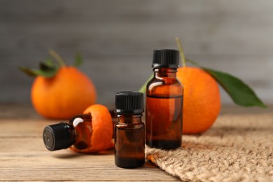 Bottles of tangerine essential oil, fresh fruit and peel on wooden table, closeup