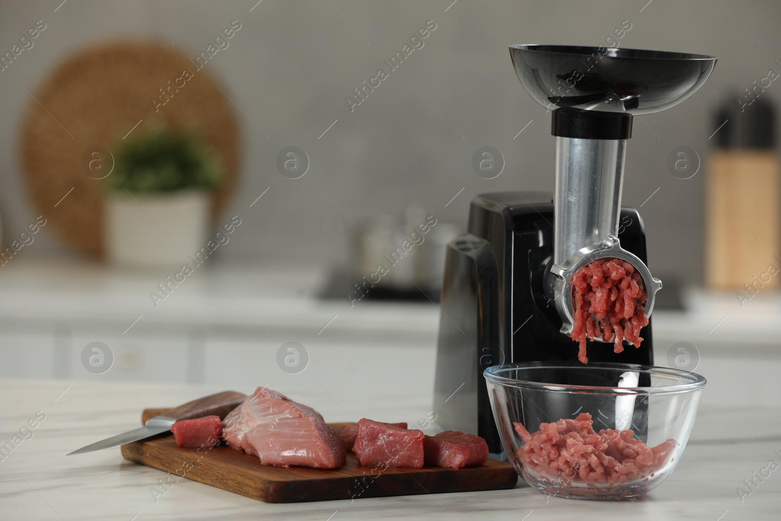 Photo of Electric meat grinder with beef mince on white table in kitchen