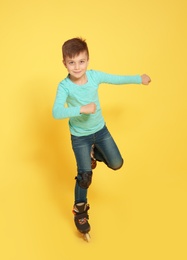 Little boy with inline roller skates on color background