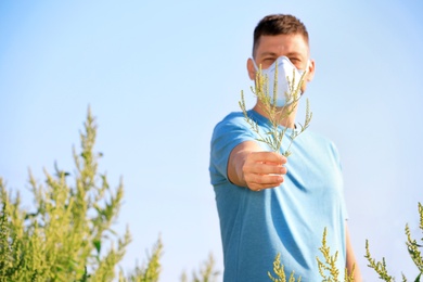 Photo of Man with ragweed branch suffering from allergy outdoors, focus on hand