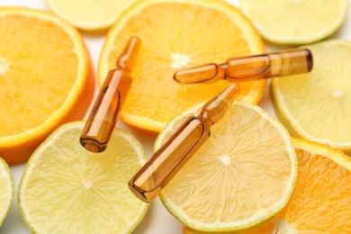 Skincare ampoules with vitamin C, lemon and orange slices on white background, closeup