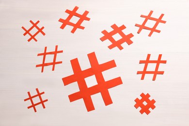 Photo of Red paper cutout symbols of hashtag on white wooden background, flat lay