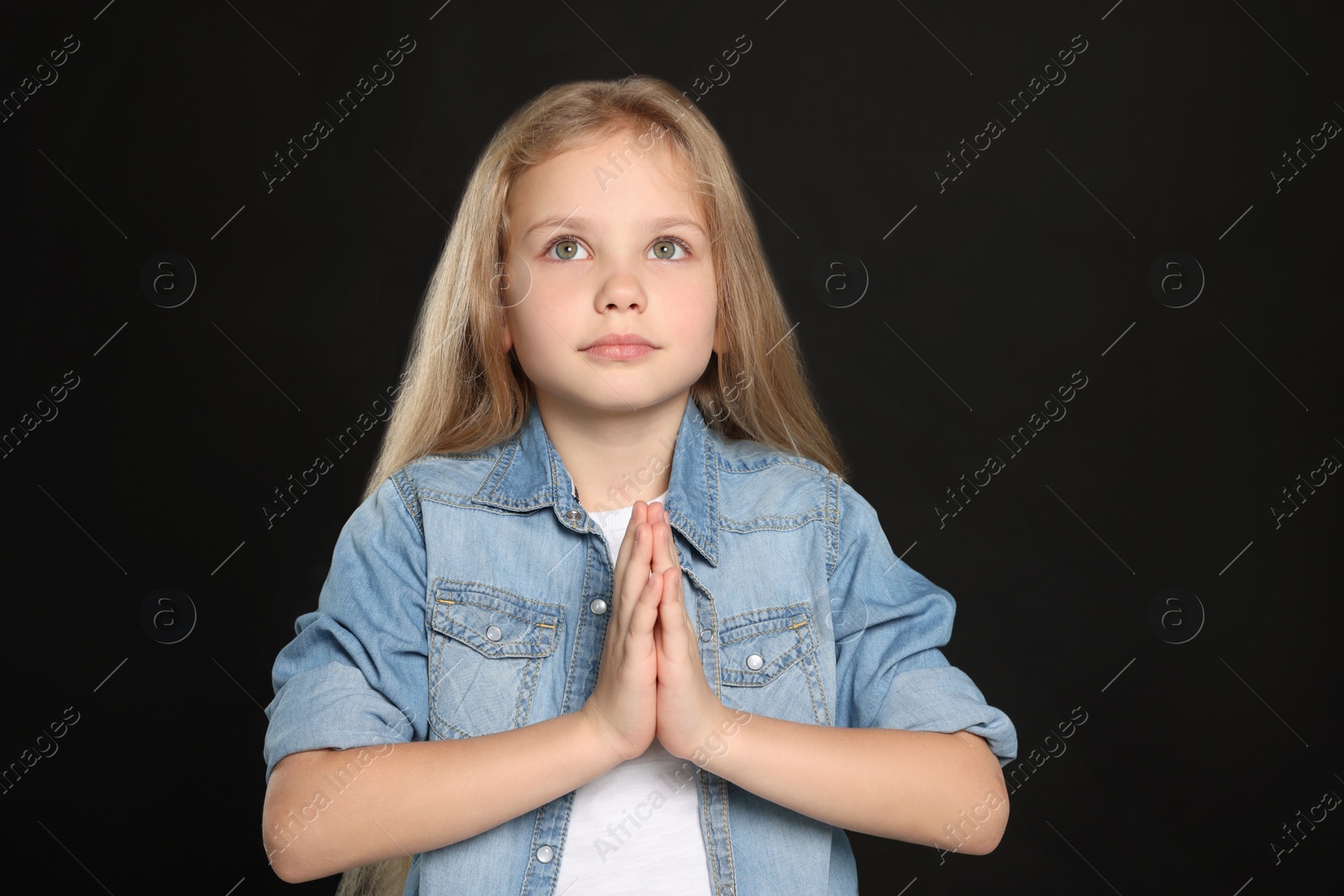 Photo of Girl with clasped hands praying on black background