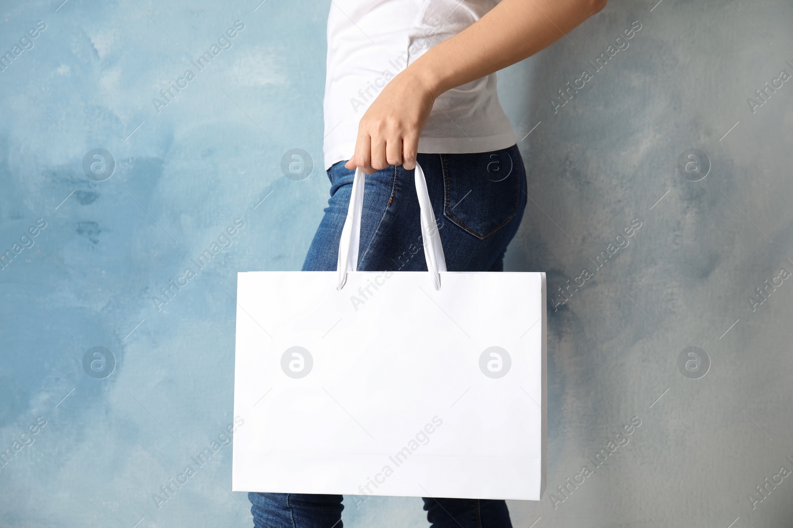 Photo of Woman holding mock-up of paper shopping bag on color background