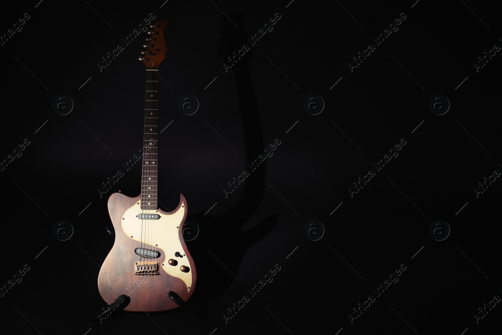 Photo of Electric guitar under spotlight on black background. Space for text