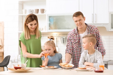 Photo of Parents and cute little children having breakfast with tasty toasted bread at table in kitchen