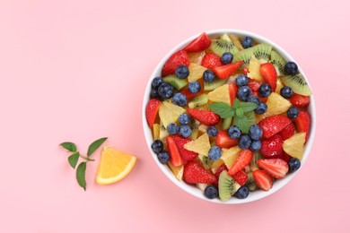 Photo of Yummy fruit salad in bowl on pink background, top view. Space for text
