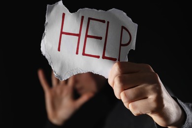 Woman holding piece of paper with word Help on black background, closeup. Domestic violence concept