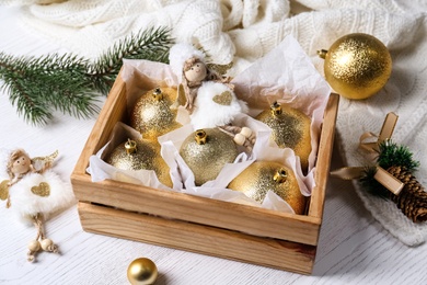 Composition with beautiful golden Christmas baubles and wooden crate on white table