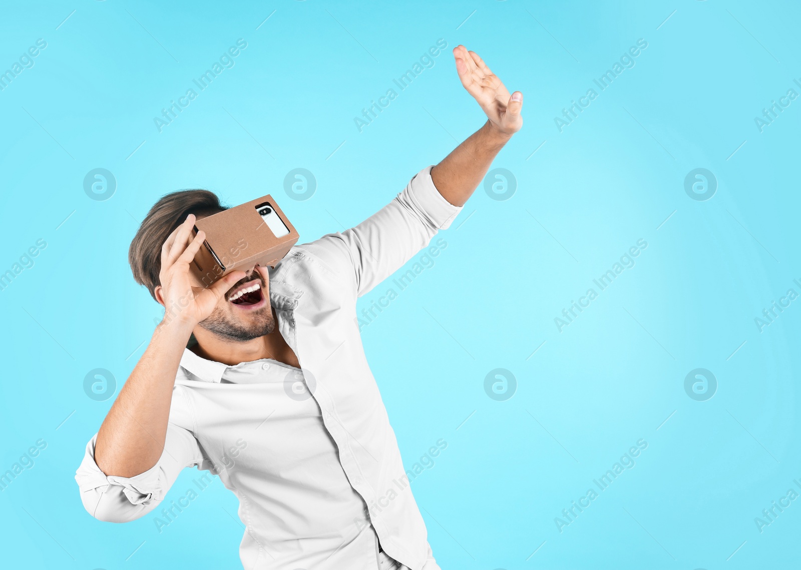 Photo of Young man using cardboard virtual reality headset on color background. Space for text